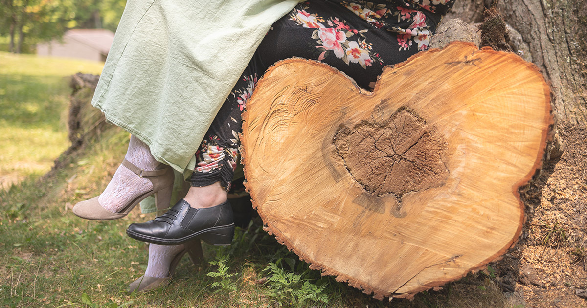 Two pairs of feet dangle over a log shaped like a heart.